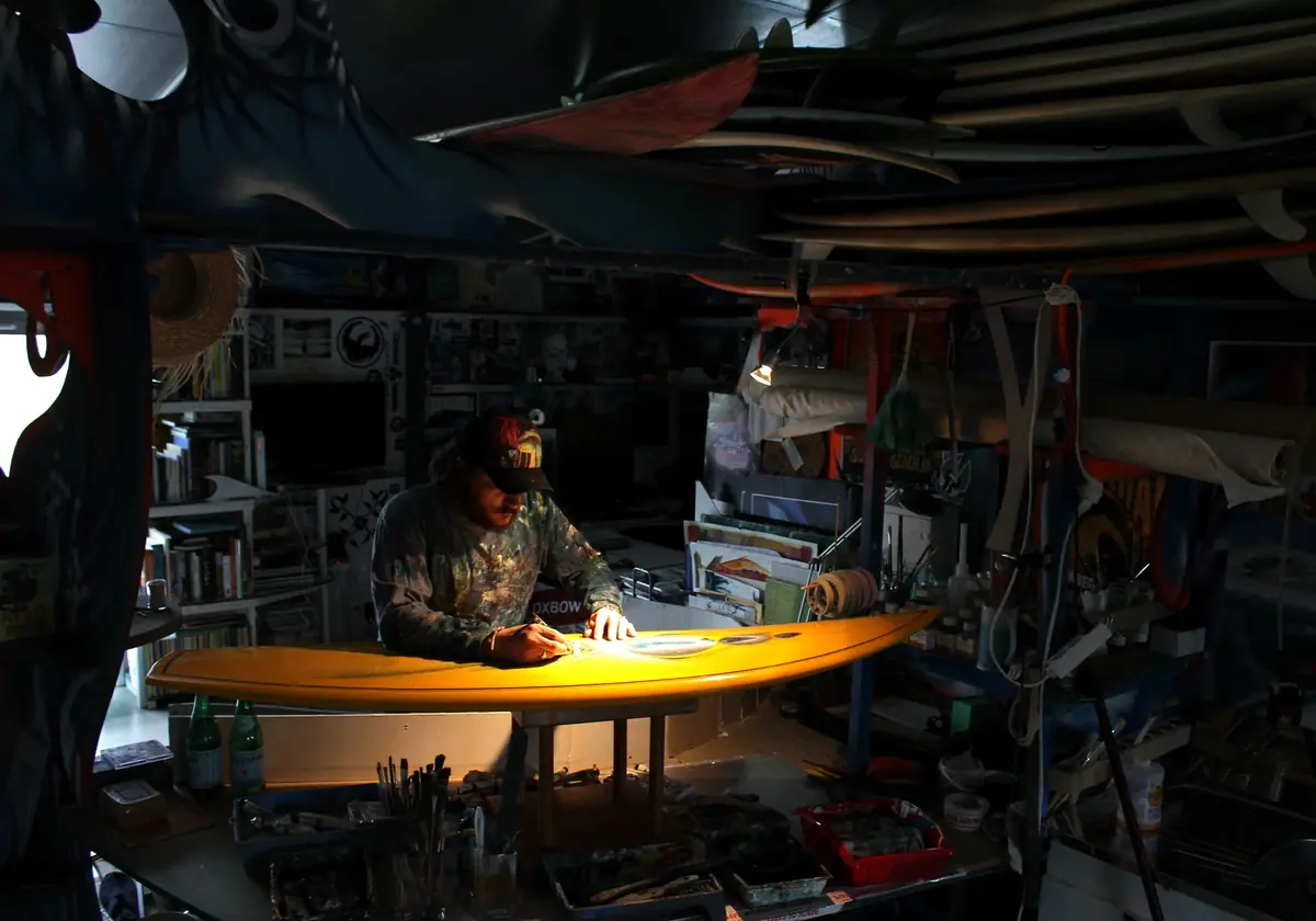 Rémi Bertoche peignant une planche de surf jaune à son établi